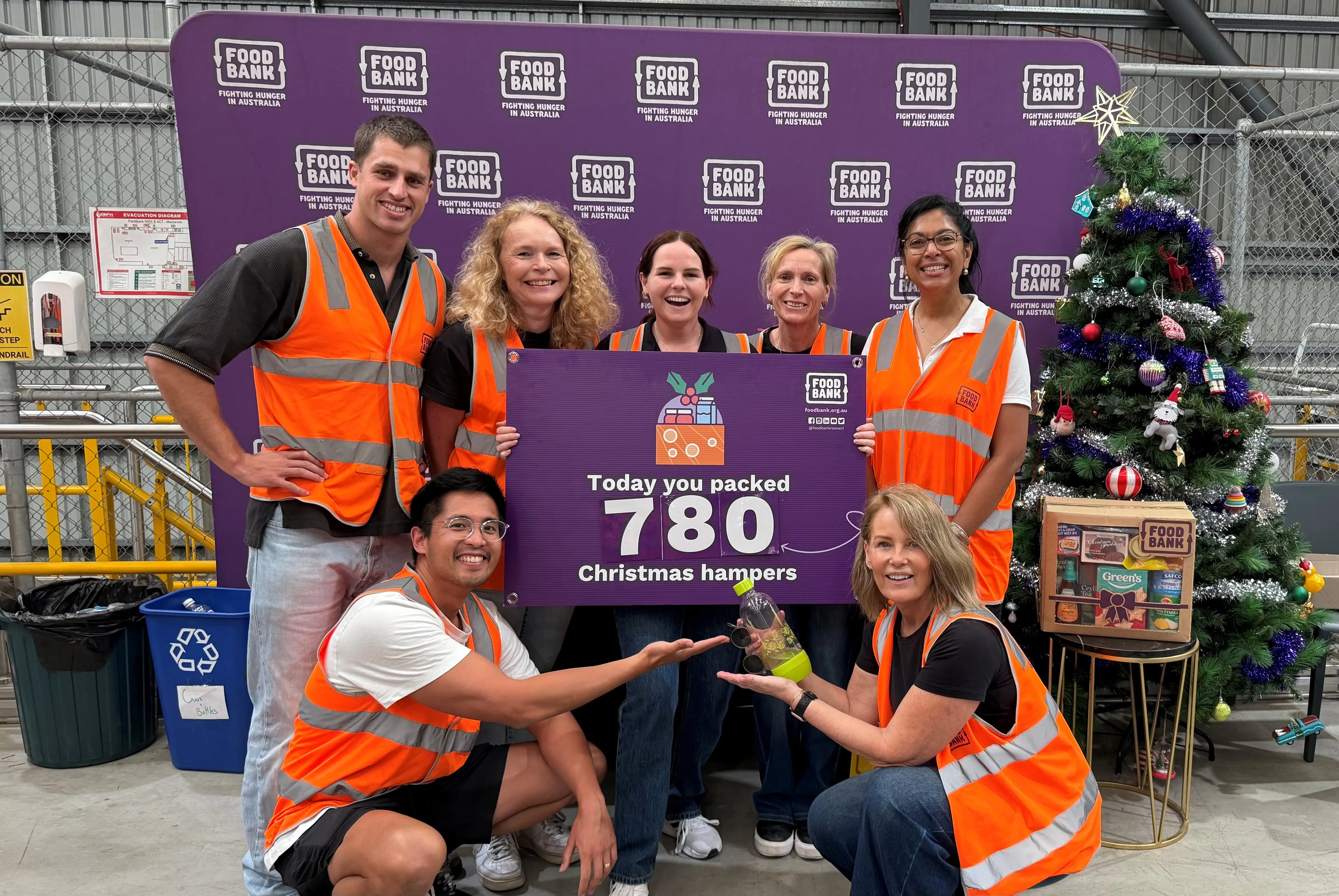 Hologic ANZ Team holding up a signage in front of a Food Bank backdrop